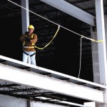 Fall arrest system using horizontal cable lifeline attached to steel beam on construction project in progress.